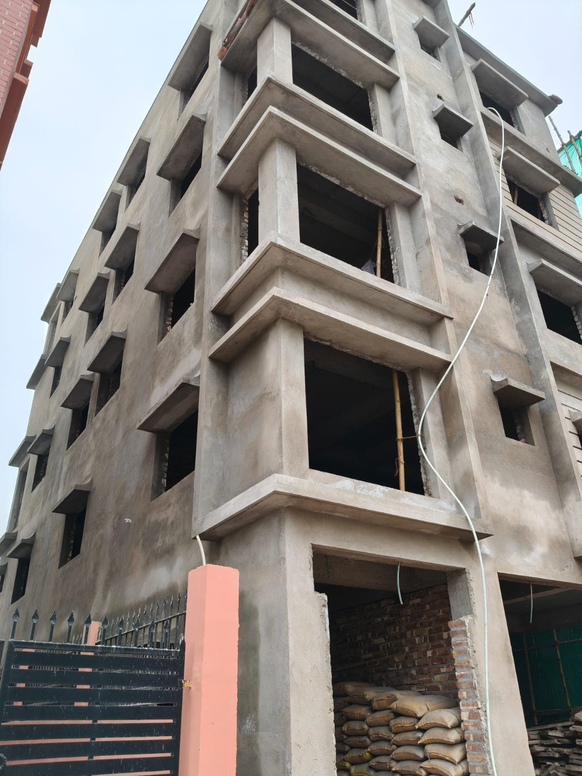 A G+4 co-operative block under construction on one of our New Town sites — RCC frame plastered, window openings still unglazed, cement stacked at ground level